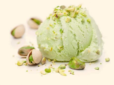 A scoop of pistachio ice cream with pistachios isolated on white background
